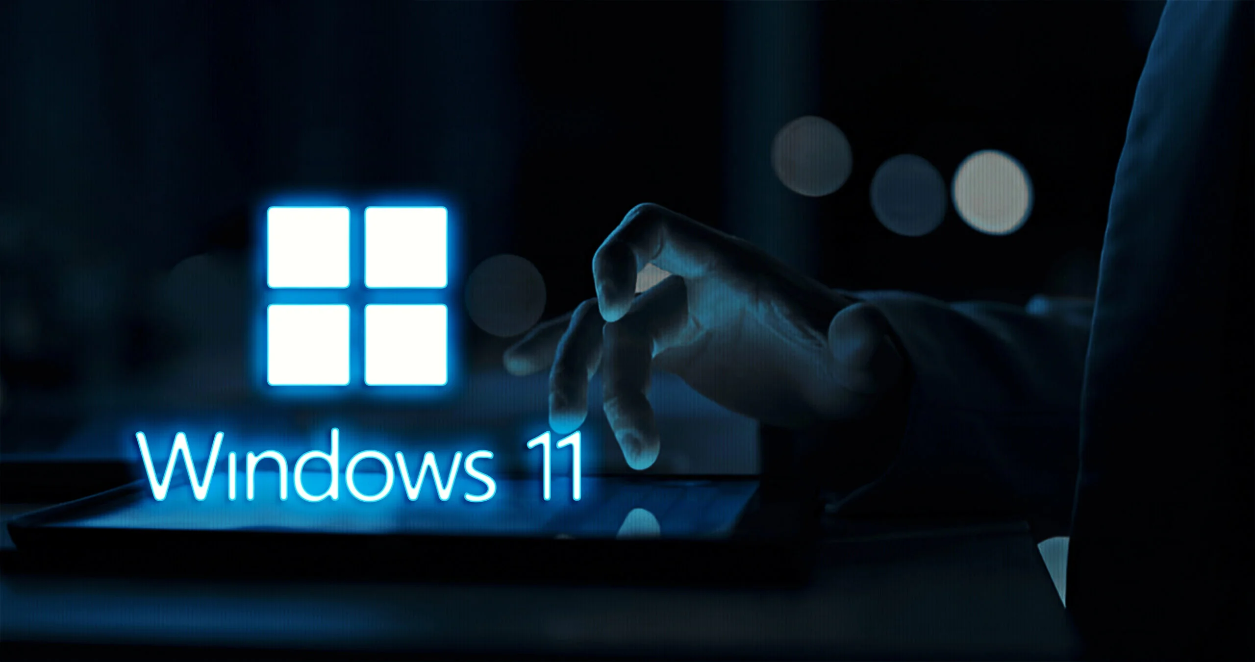 Hand interacting with a tablet displaying the Windows 11 logo in a dark, professional setting